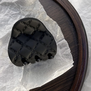 Detail shot of a matte black quilted hair claw clip on a rustic wooden tray