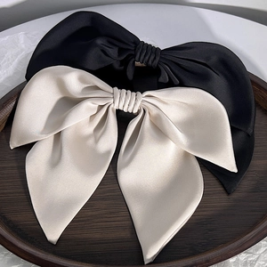 Detail of elegant black and beige satin bow hair clips on a minimalist wood tray