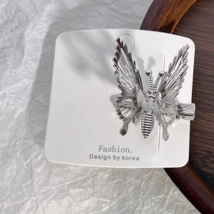 Close-up of silver hollow butterfly hair clip with metallic wings on display card