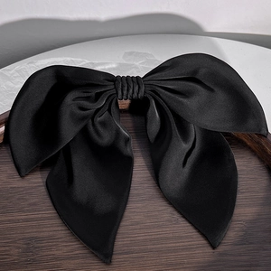 Close-up of large black satin bow hair clip with double ribbons on a vintage wooden tray