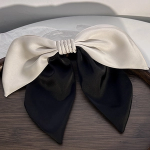 Close-up of elegant silk satin bow hair clip in silver and black on a wooden tray