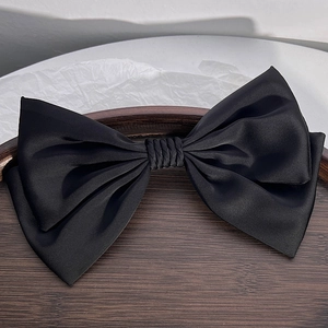 Close-up of a large black satin bow hair clip with a smooth glossy texture in a tray