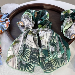 Detail of floral chiffon scrunchie with ribbons on dark wooden tray showing green edges