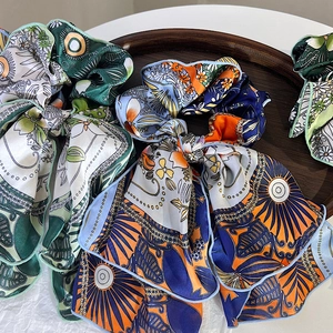 Detail of silk-feel chiffon scrunchies with floral and sun patterns in a wooden tray