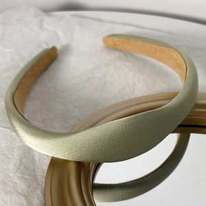 Close-up of a padded light green satin headband with silk texture on a golden mirror