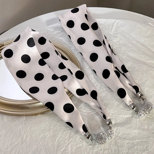 Close-up of polka dot silk scarf with luxury rhinestone metal charms on white textured paper