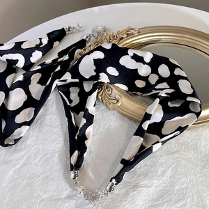 Détail d'un foulard en satin noir à pois avec fermoir magnétique orné de faux diamants