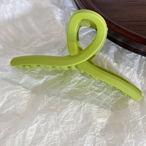 Close-up of a matte avocado green large hair claw clip with cross-twist design