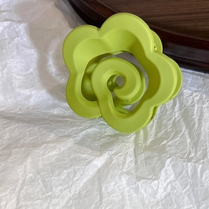 Close-up of matte green flower claw clip with spiral center on a wooden tray