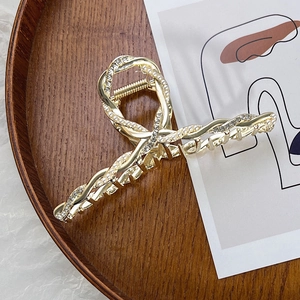 Dettaglio di grande molletta dorata a spirale con perle bianche e strass scintillanti