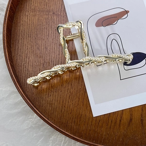 Vista dettagliata della grande molletta per capelli dorata con perle e design a treccia
