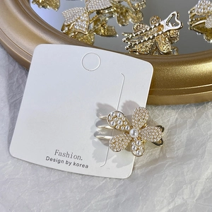 Detailed macro view of golden flower hair claw with white pearl inlay on display card