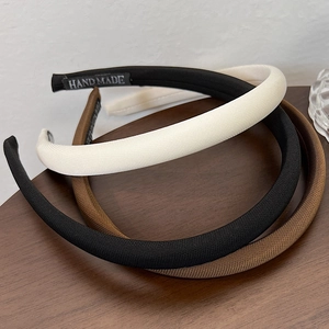 Detail of three narrow fabric headbands in black, beige, and brown with handmade label