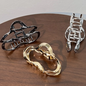 Elegant wavy hollow metal hair claws in gold, silver, and black on wooden surface