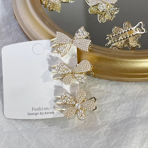 Close-up of golden pearl hair clips set featuring butterfly and flower designs on white texture