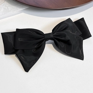 Detail view of a large black satin bow hair clip with layered fabric texture and silk finish