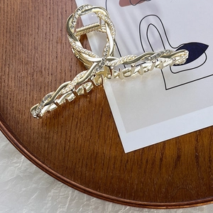 Elegante pinza per capelli in lega dorata con perle e strass su un vassoio di legno scuro