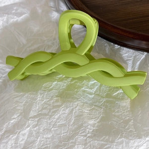 Close-up of a matte bright green hair claw clip with a twisted chain design on white paper