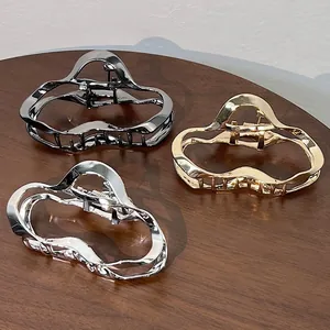 Close-up of three metallic hair claws in gold, silver, and black on a wooden table