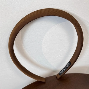 Detail of the brown fabric headband featuring a black woven HAND MADE tag on the inner side