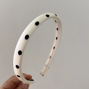 Détail rapproché du serre-tête en tissu blanc à gros pois noirs tenu à la main