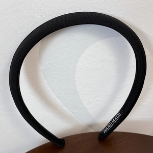 Close-up of black fabric padded headband with a handmade label on wooden surface