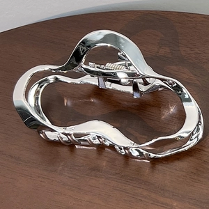 Detail view of silver metal hair claw with modern irregular wavy lines and mirror finish