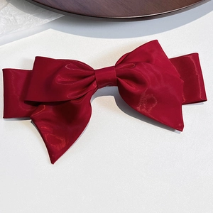 Detail shot of a wine red satin fabric bow hair clip on a minimalist white background