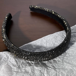 Dettaglio del cerchietto imbottito largo con strass neri brillanti su sfondo scuro