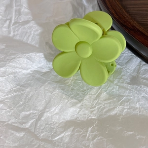 Detail shot of the matte light green flower hair claw clip on a rustic wooden tray