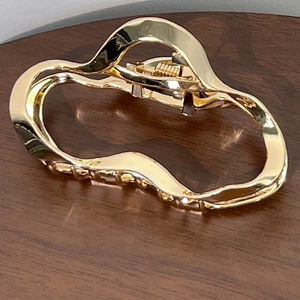 Detail of a wavy gold metal hair claw clip with a glossy finish and strong spring mechanism