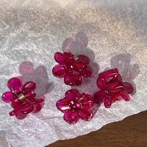 Close-up of four mini flower hair claws in translucent dark pink with silver metal spring