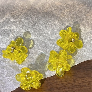 Close-up of four mini translucent yellow flower hair claws on textured white paper