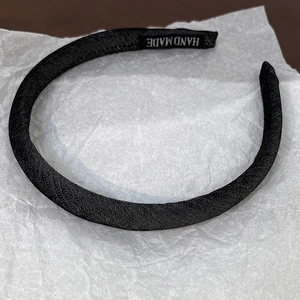Detailed macro view of black fabric headband with handmade label on white textured paper