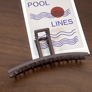 Detail of a large matte dark grey shark hair claw clip with strong metal spring on wood