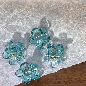 Detail of four transparent blue flower hair claws made of acrylic on white paper