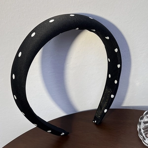 Détail d'un serre-tête vintage noir à pois blancs posé sur une surface en bois foncé