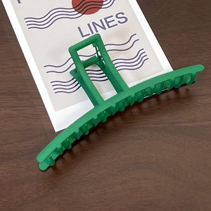 Detail showing the matte green large hair claw clip on a textured wooden background