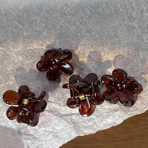 Close-up of four mini flower hair claws in amber resin on a soft white paper background