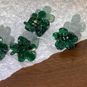 Close-up of mini flower hair claw in dark green resin with golden spring on paper