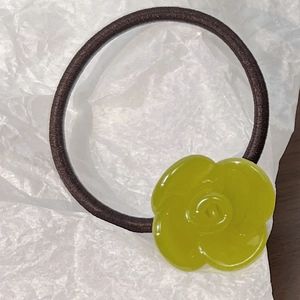 Close-up of a green resin camellia flower charm on an elastic brown hair tie band