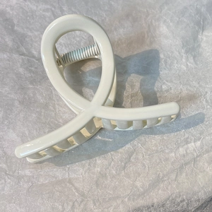 Detail of a creamy white large hair claw clip with a crossover design and metal spring