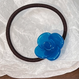 Detail of blue resin camellia flower hair tie with durable brown elastic cord