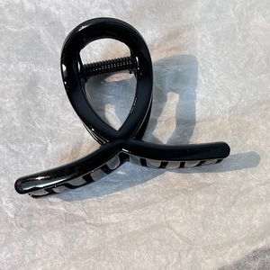 Detail of glossy black hair claw clip with cross-twist design on white paper background