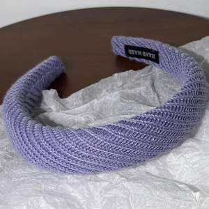 Détail d'un bandeau en maille violette avec un motif torsadé épais et étiquette faite main