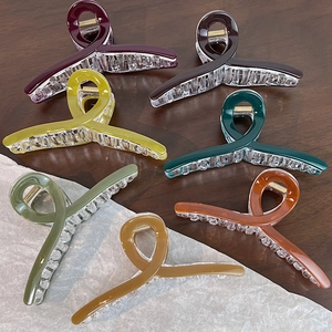Dettaglio di grandi mollette per capelli da 13 cm in sette colori caramella su legno scuro