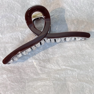 Dettaglio di un fermaglio per capelli marrone scuro lucido con denti trasparenti e molla d'oro