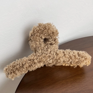 Gros plan d'une pince à cheveux en peluche caramel à texture douce sur bois sombre