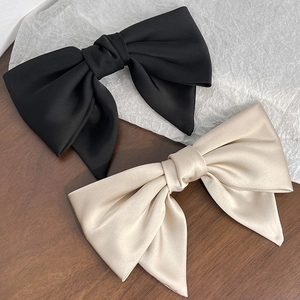 Close-up of silk satin bow hair clips in black and champagne on a soft textured background