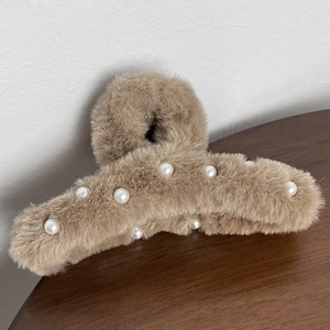 Close-up of brown plush hair claw clip with white faux pearls on a wooden surface